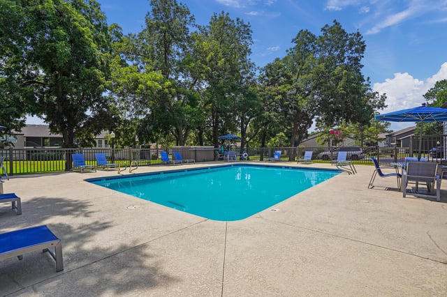 Outdoor swimming pool with blue lounge chairs and umbrellas.