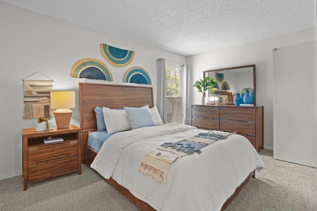 Stylish bedroom with a wooden bed, nightstand, and dresser. Features woven wall art and a large mirror.