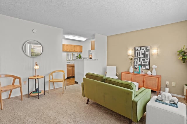 Living room with a green sofa, accent chairs, and a view of the kitchen.