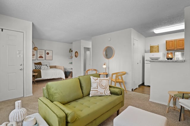 Stylish living room with a green sofa, ottoman, and view into a bedroom.