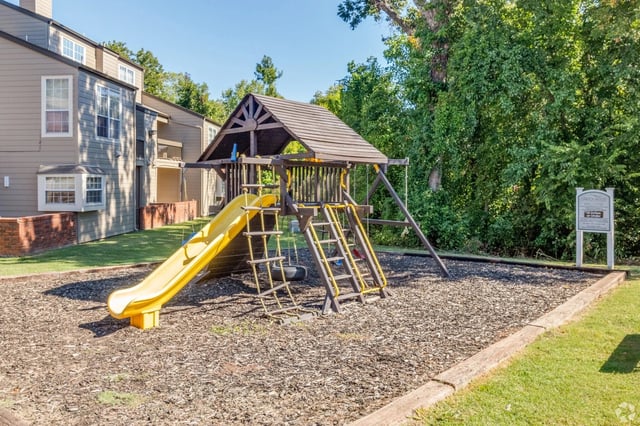 Playground with slide, swings, and climbing ladder next to apartment buildings.