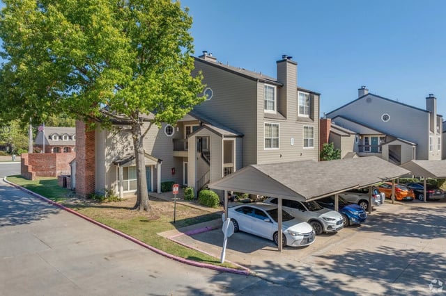 Apartment building exterior with covered parking and mature trees.