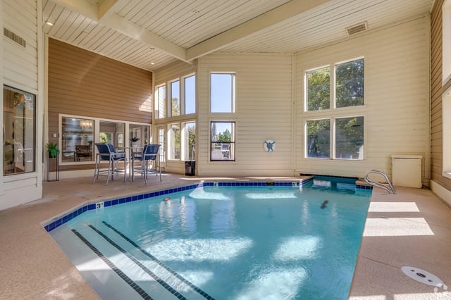 Indoor swimming pool with large windows and seating area.