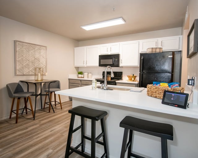 Modern kitchen with white countertops, black appliances, and a breakfast bar with stools.