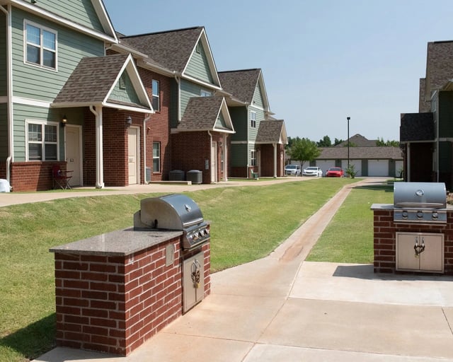Row of apartment townhomes with brick and green siding, grills, and a grassy courtyard.
