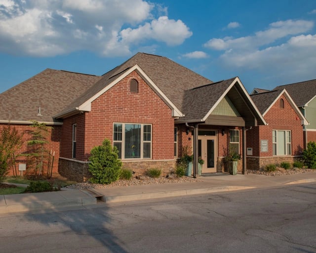 Exterior view of a brick apartment community building with front entrance and landscaping.