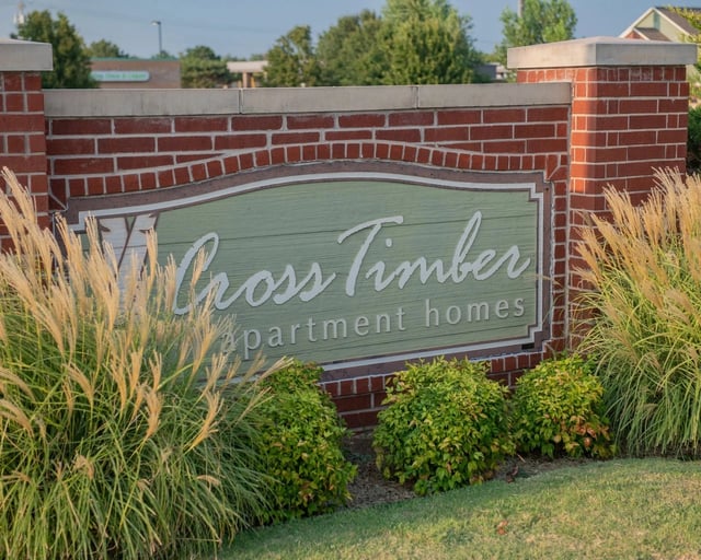 Exterior brick monument sign reading 'Cross Timber Apartment Homes' with ornamental grasses around.