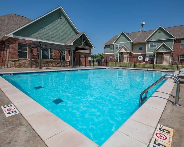Outdoor community pool with blue water, metal handrail, and surrounding residential buildings.