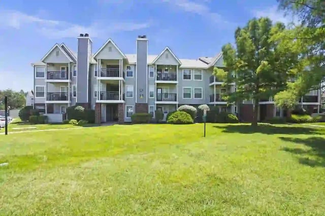 Image of a multi-story apartment building with green grass and trees in the foreground.