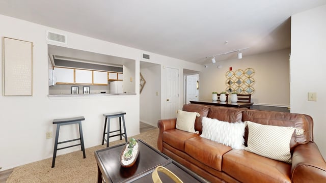 Living room with brown leather sofa, coffee table, dining table, and bar stools in front of kitchen counter.