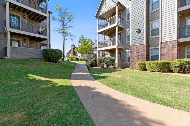 Winding walkway leading past apartment buildings with balconies and manicured lawns.