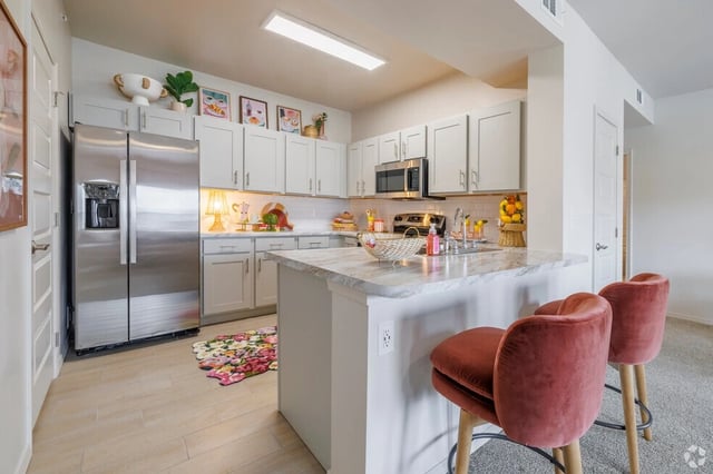 Modern kitchen with stainless steel appliances, white cabinets, and a marble island with bar stools.
