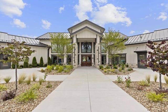 Front entrance of an apartment community with stone columns, glass doors, and desert landscaping.