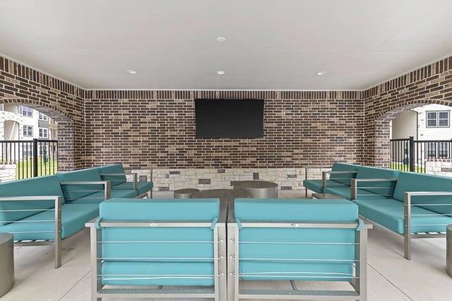 Covered brick-walled outdoor lounge with teal seating and a wall-mounted TV.