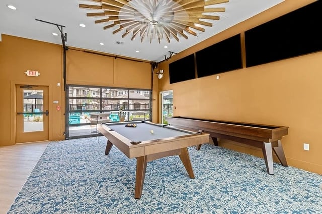Interior community recreation room with a pool table, shuffleboard, and large glass doors.