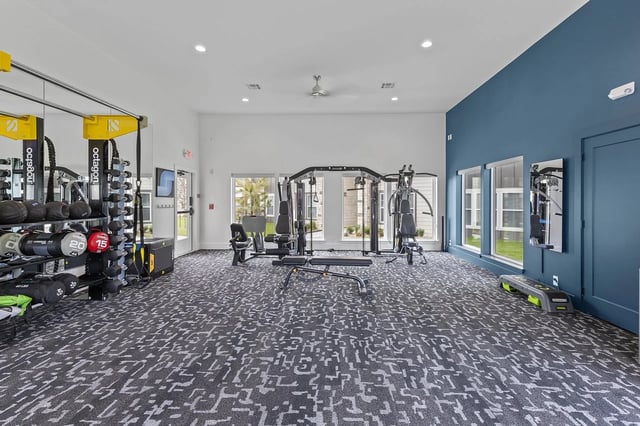 Interior view of a modern apartment community gym with free weights, weight machines, and benches.