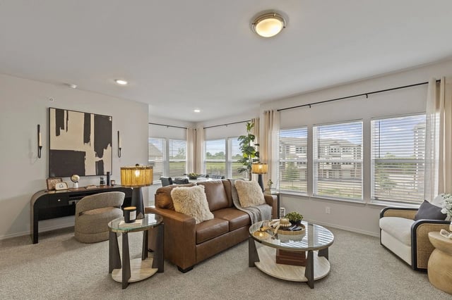 Bright living room with brown leather sofa, glass coffee and side tables, and large windows.
