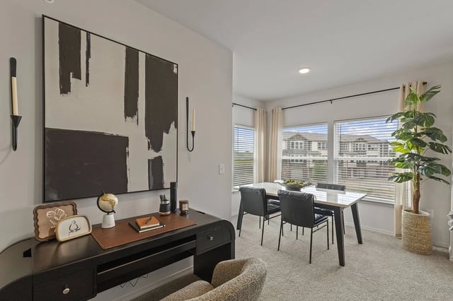 Interior apartment space with a desk, abstract wall art, and a dining table by large windows.