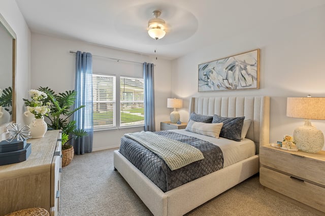 Bedroom with a king-size bed, dresser, and large windows.