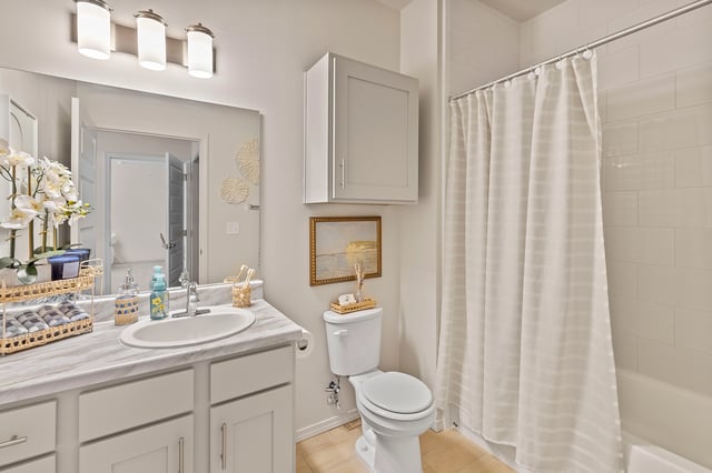 A modern bathroom with a marble vanity, toilet, and bathtub with a white shower curtain.