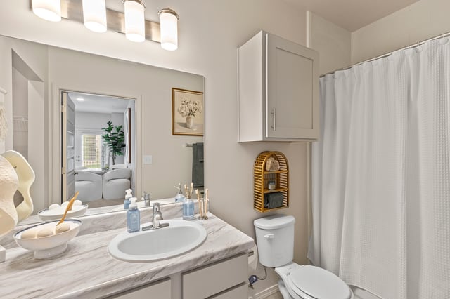 Modern bathroom with a vanity, sink, toilet, and shower with white curtain.