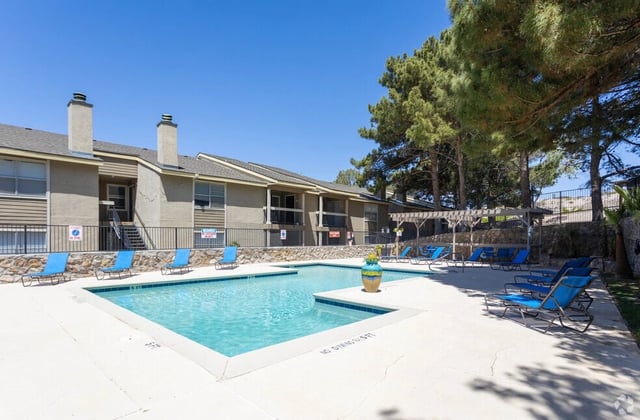 Outdoor swimming pool with lounge chairs and surrounding apartment buildings on a sunny day.