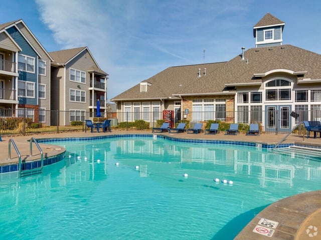 Bright blue swimming pool with lounge chairs and apartment buildings in the background.