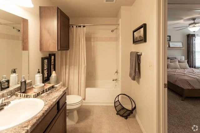 Modern bathroom with vanity, toilet, and tub with shower curtain. Adjacent bedroom visible.