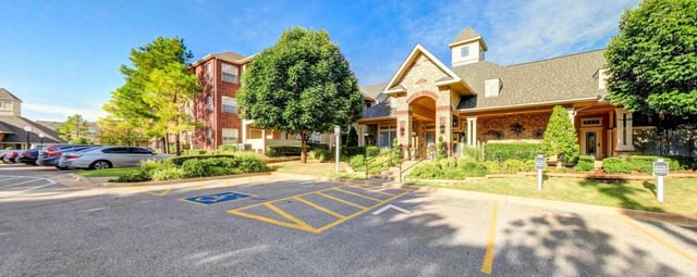 Exterior of apartment building with parking lot and landscaping.