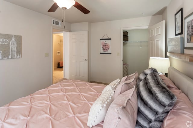 Bedroom with a pink comforter and decorative pillows on the bed, a ceiling fan, and a closet.