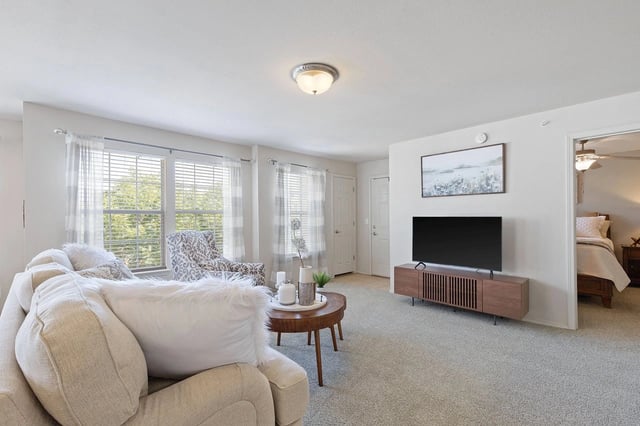 Bright living room with beige sofa, patterned chair, round coffee table, and a TV.