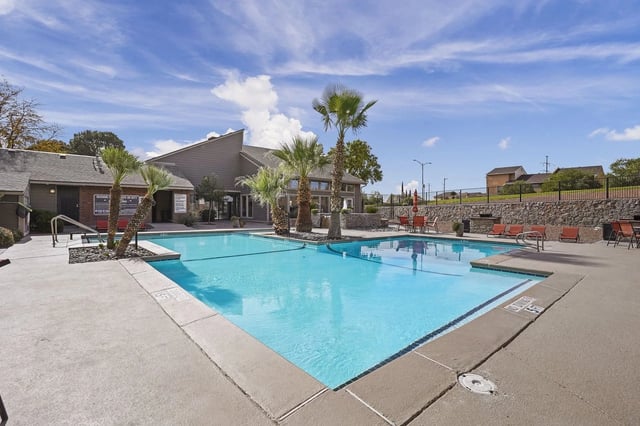 Swimming pool and lounge chairs with palm trees and apartment buildings in the background.