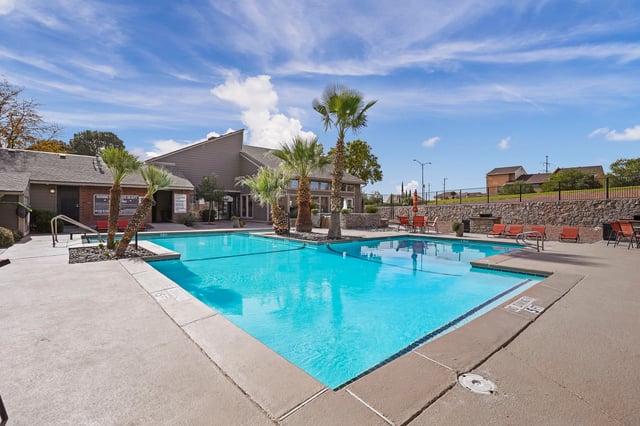 Resort-style swimming pool with lounge chairs and palm trees.
