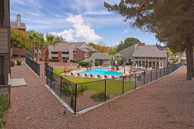 Resort-style swimming pool and lounge area with palm trees and surrounding apartment buildings.