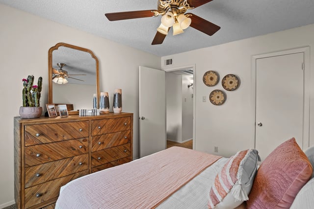 A bedroom with a dresser, mirror, bed, and ceiling fan.