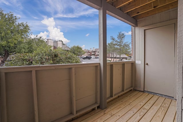 View from a balcony with a door to the right and overlooking trees and apartment buildings.