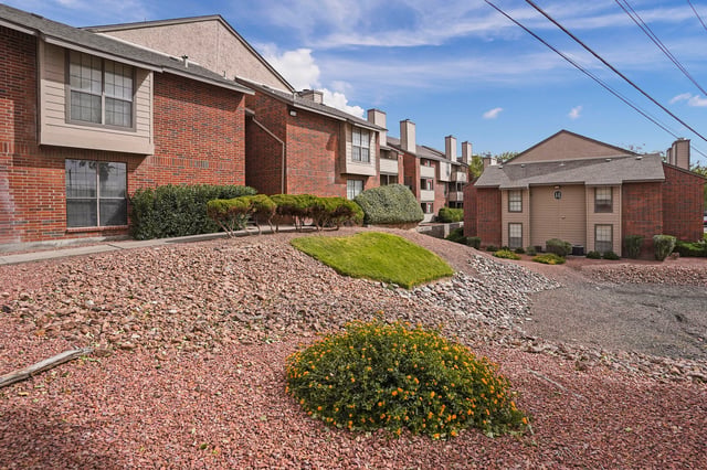 Exterior view of brick apartment buildings with landscaping and a blue sky.