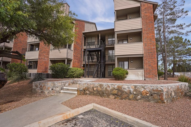 Exterior of an apartment building with brick and beige siding, featuring balconies and an external staircase.