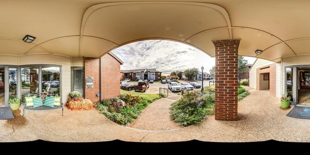 Exterior view of apartment buildings and entrance area with seating and landscaping.