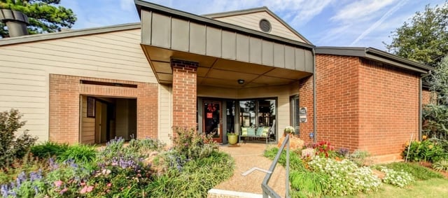 Exterior building entrance with brick and siding, flower beds, and seating.