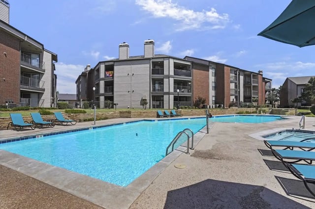 Apartment complex with a large swimming pool and lounge chairs.