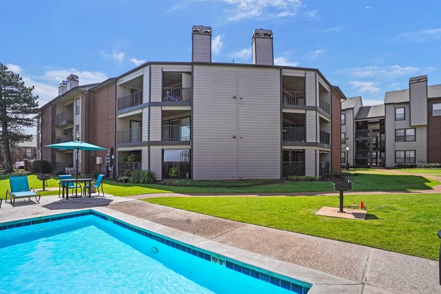 Outdoor swimming pool with lounge chairs and a picnic table near an apartment building.