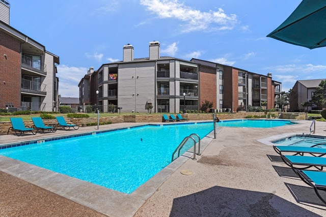 Resort-style swimming pool and spa area with lounge chairs and apartment buildings in the background.