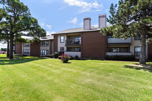Exterior view of apartment buildings with manicured lawns and trees.