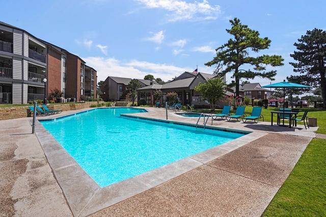 Outdoor swimming pool with lounge chairs and a table with an umbrella.
