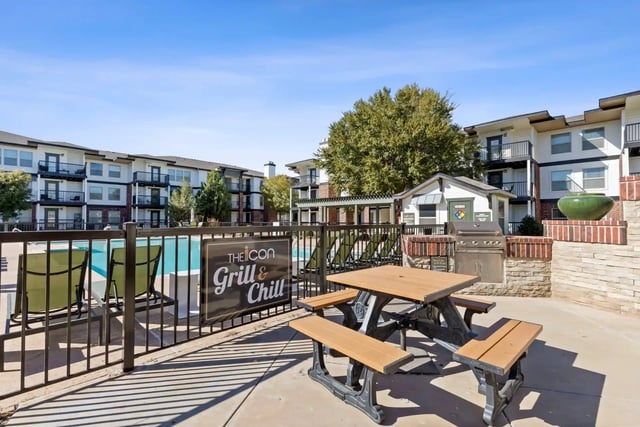 Outdoor community grill area with a picnic table and pool in the background.