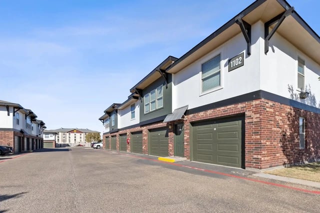 Row of two-story townhomes with brick bases and attached garages along a wide street.
