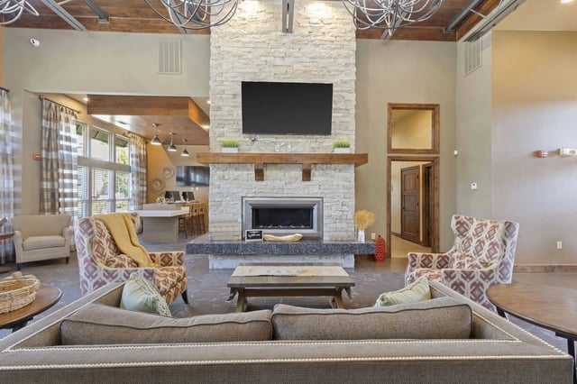 Community lounge with a stone fireplace, mounted TV, and multiple seating areas.