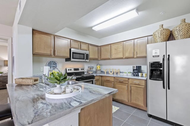 Kitchen in an apartment with wooden cabinets, granite counters, island, and stainless-steel appliances.