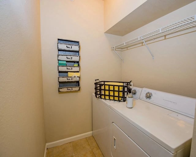 Laundry closet with a white washer and dryer, a wire shelf, and a labeled organizer.